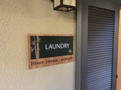 photo of a large dark green laundry room sign on a bamboo backplate with the hours of operation burned into the wood 